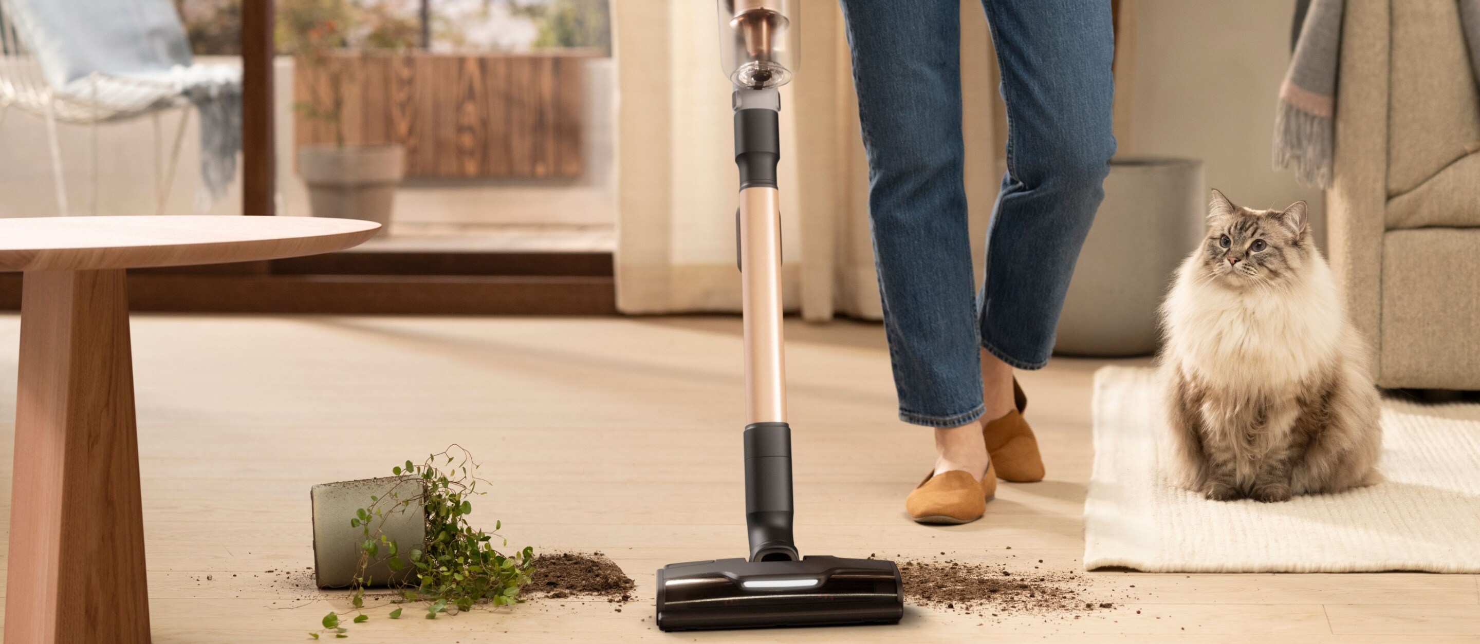 Woman vacuuming floor in a living room with a cat next to her.