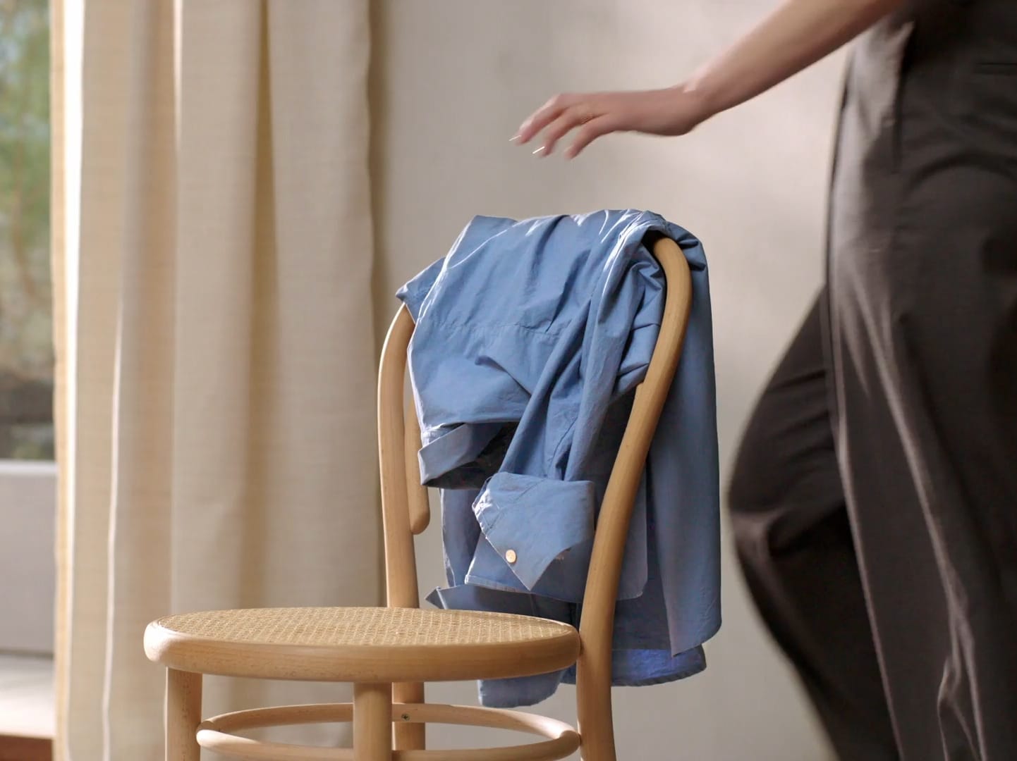 Woman hanging a blue shirt over the back of a chair.